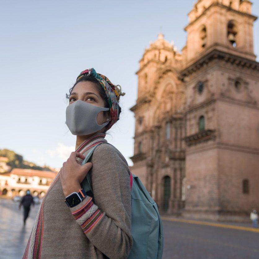 Portrait of a happy woman sightseeing around Cusco while wearing a facemask - travel during the COVID-19 pandemic concepts